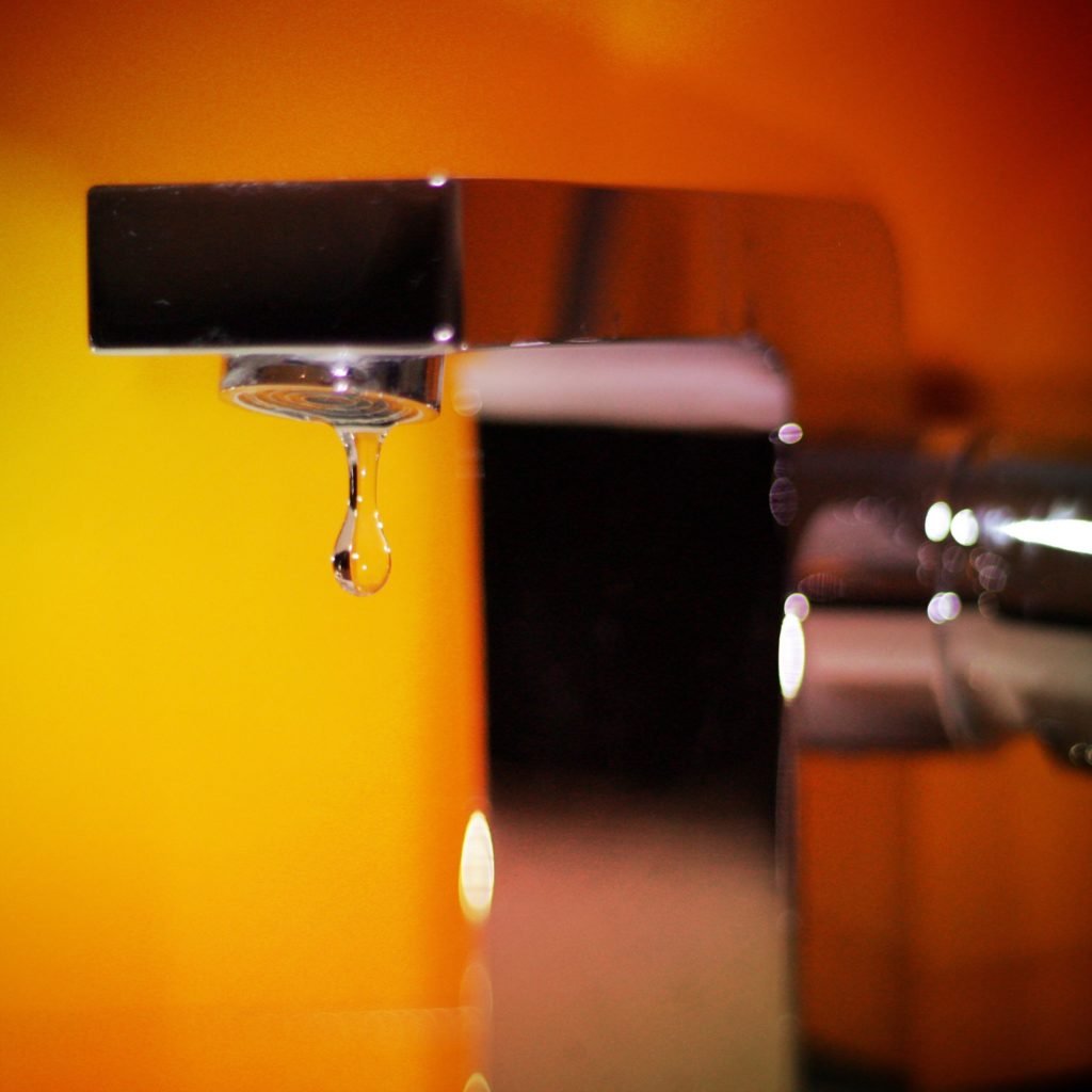 Water drop of a leaking faucet on the orange background